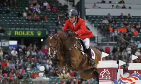 Rider in a red coat jumping at the Rolex arena